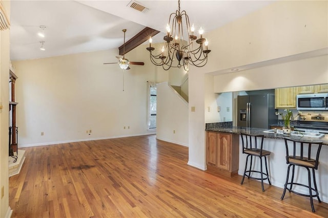 kitchen featuring a breakfast bar area, ceiling fan, vaulted ceiling with beams, stainless steel appliances, and light hardwood / wood-style floors