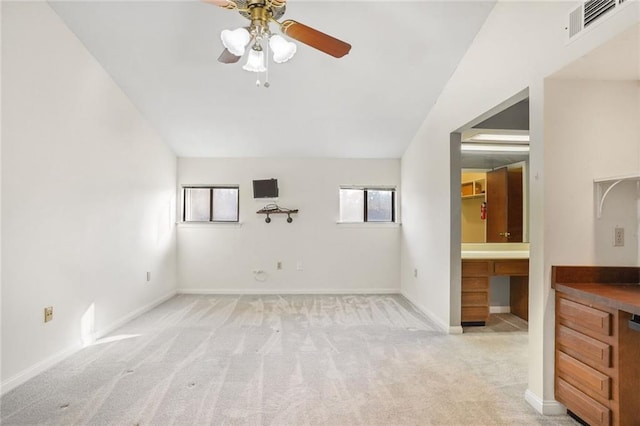 carpeted empty room with built in desk, ceiling fan, and vaulted ceiling