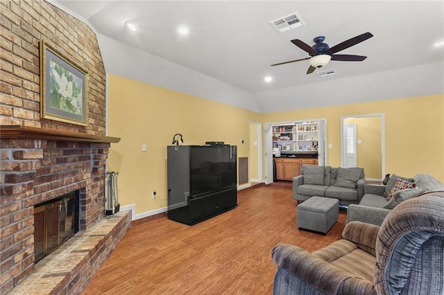 living room with a brick fireplace, vaulted ceiling, ceiling fan, and light wood-type flooring