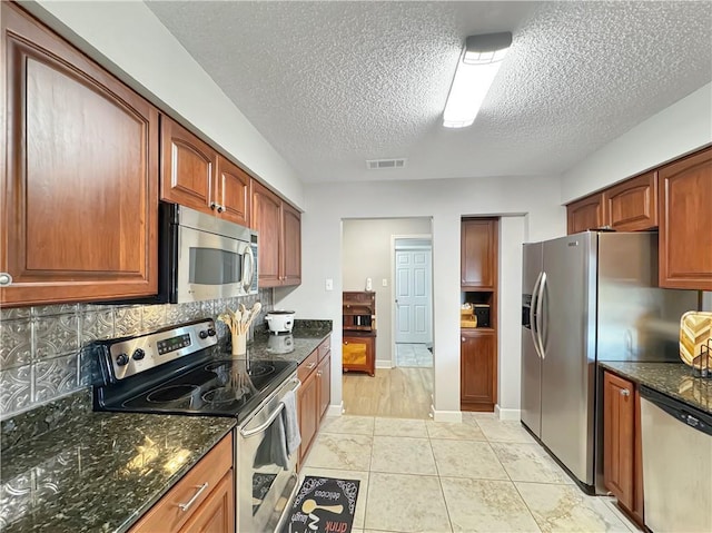 kitchen featuring appliances with stainless steel finishes, a textured ceiling, decorative backsplash, and dark stone countertops