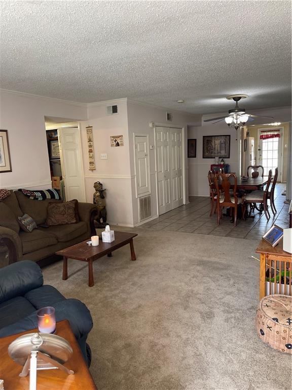 carpeted living room with crown molding, ceiling fan, and a textured ceiling