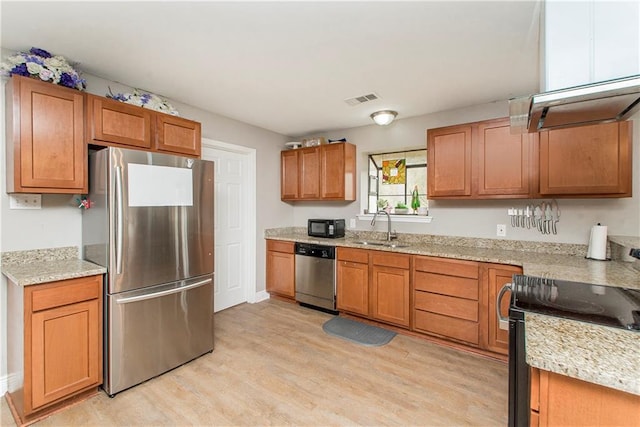 kitchen with sink, stainless steel appliances, light hardwood / wood-style floors, and light stone countertops