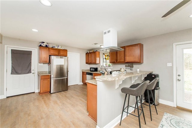 kitchen with a breakfast bar, kitchen peninsula, stainless steel appliances, plenty of natural light, and light hardwood / wood-style flooring