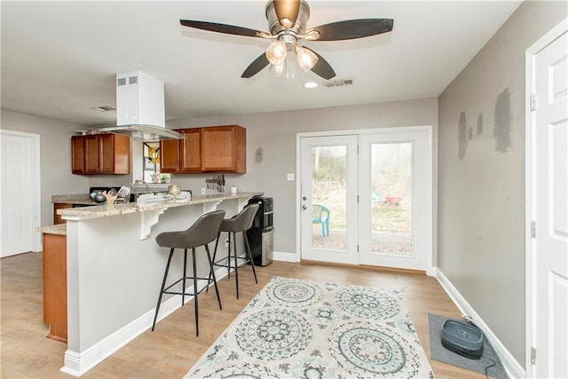 kitchen with a breakfast bar, island exhaust hood, light stone counters, kitchen peninsula, and light wood-type flooring