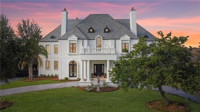 back of property with a chimney, a lawn, a balcony, and stucco siding