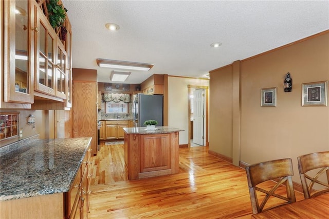 kitchen with sink, stainless steel refrigerator, a center island, dark stone counters, and light wood-type flooring