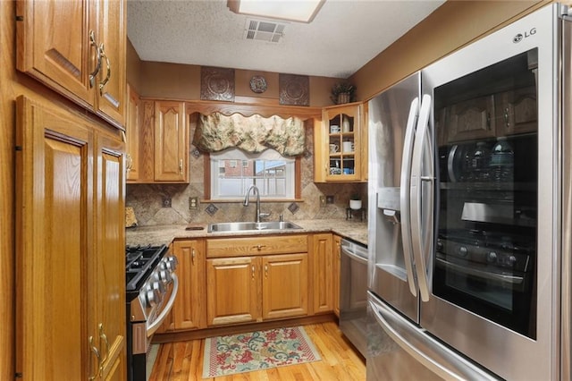 kitchen featuring appliances with stainless steel finishes, light stone countertops, sink, and light wood-type flooring