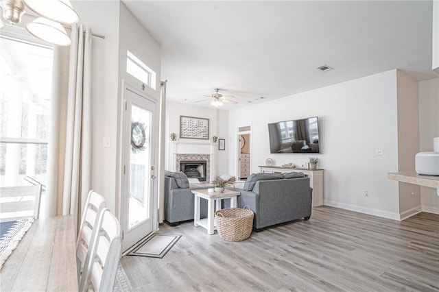 living room featuring light wood-style floors, visible vents, a fireplace, and a ceiling fan