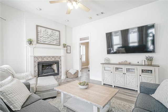 living area with ceiling fan, a fireplace, visible vents, baseboards, and light wood-type flooring