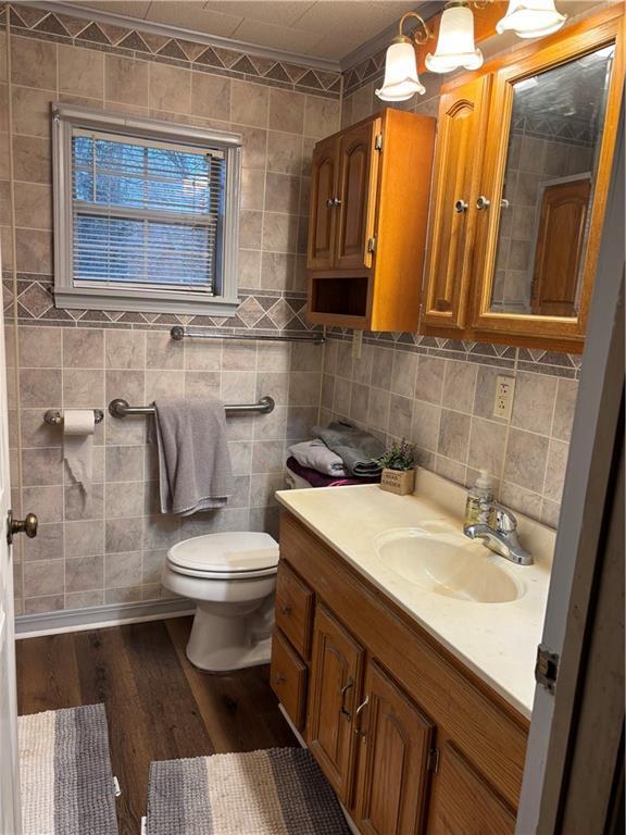 bathroom with toilet, wood finished floors, vanity, tile walls, and decorative backsplash