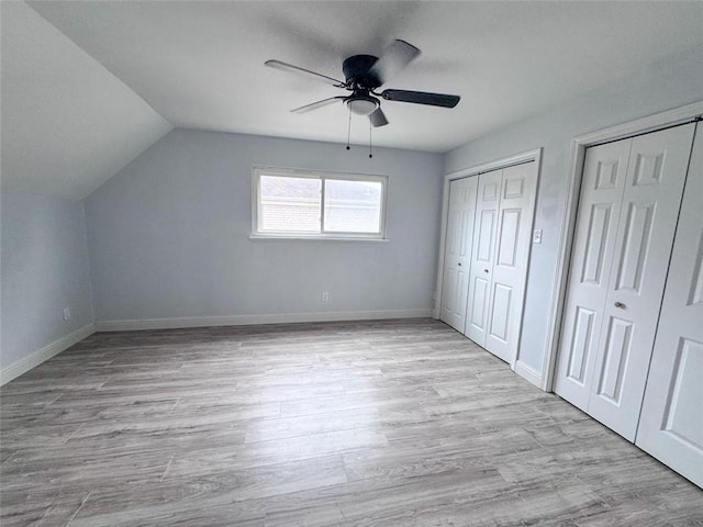 unfurnished bedroom with lofted ceiling, ceiling fan, light wood-style flooring, baseboards, and multiple closets