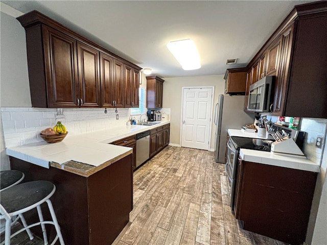 kitchen featuring dark brown cabinets, a kitchen breakfast bar, kitchen peninsula, and appliances with stainless steel finishes