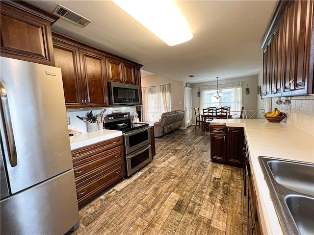 kitchen with appliances with stainless steel finishes, sink, decorative backsplash, hanging light fixtures, and dark wood-type flooring