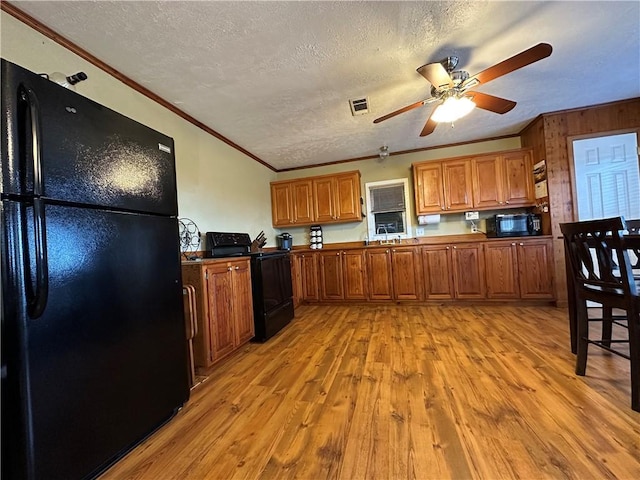 kitchen featuring crown molding, black appliances, a textured ceiling, and light wood-type flooring