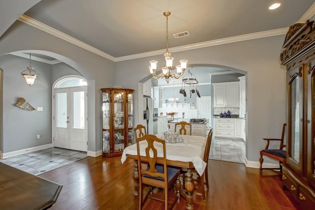 dining space featuring dark wood-type flooring, crown molding, an inviting chandelier, and french doors