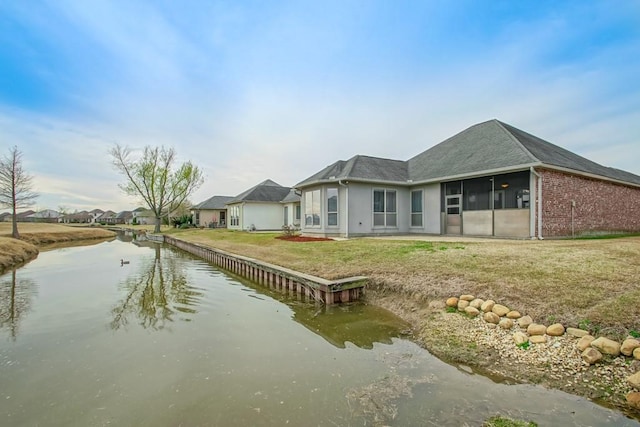 back of property featuring a water view, a sunroom, and a lawn