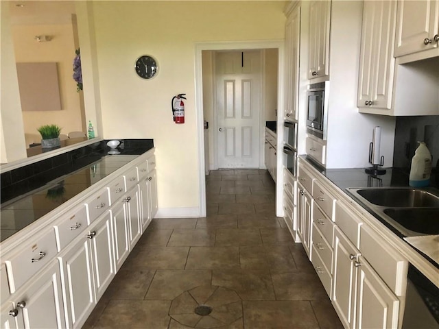 kitchen with white cabinetry, sink, stainless steel microwave, and dark tile patterned flooring