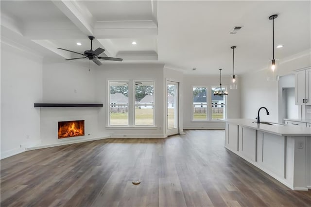 unfurnished living room featuring sink, crown molding, dark wood-type flooring, and a healthy amount of sunlight