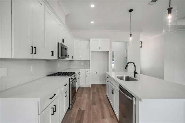 kitchen featuring appliances with stainless steel finishes, pendant lighting, white cabinetry, an island with sink, and sink