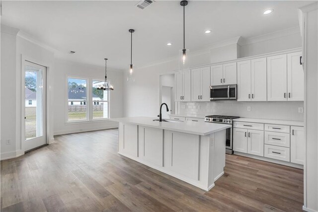 kitchen with an island with sink, appliances with stainless steel finishes, white cabinets, and decorative light fixtures