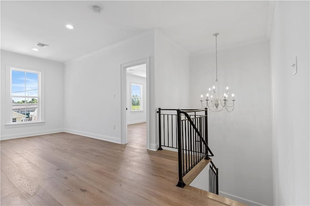 unfurnished room featuring a notable chandelier, a wealth of natural light, ornamental molding, and hardwood / wood-style floors