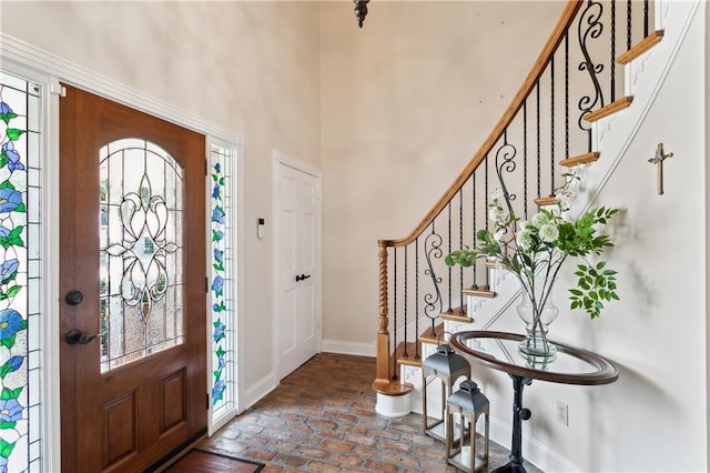 foyer entrance featuring brick floor, a high ceiling, and baseboards