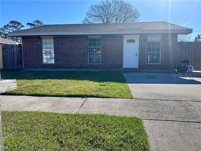 single story home with brick siding, a front yard, fence, and a shingled roof