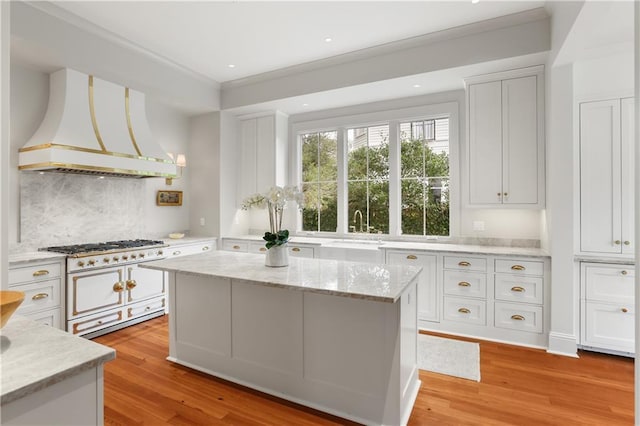 kitchen featuring light hardwood / wood-style flooring, double oven range, a center island, custom range hood, and white cabinets