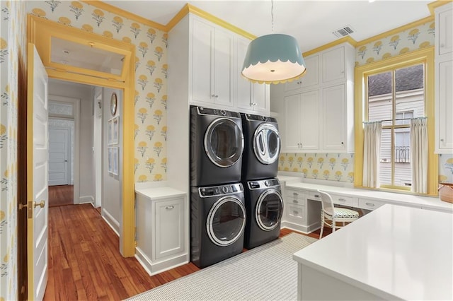 clothes washing area featuring stacked washer / drying machine, hardwood / wood-style flooring, washer and clothes dryer, and cabinets