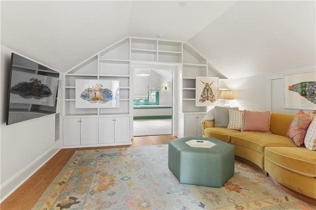 living room featuring lofted ceiling, built in shelves, and light hardwood / wood-style flooring