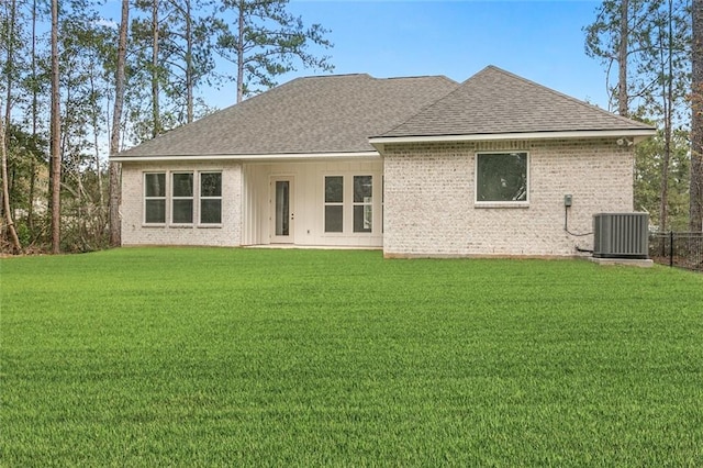 rear view of property with roof with shingles, central air condition unit, a lawn, and brick siding