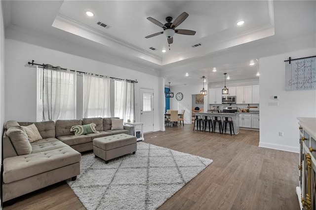 living room with crown molding, a tray ceiling, and light hardwood / wood-style floors