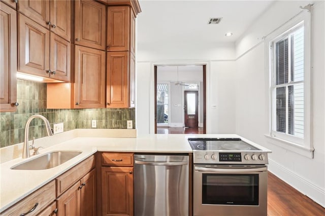 kitchen with dark wood-type flooring, sink, appliances with stainless steel finishes, kitchen peninsula, and backsplash