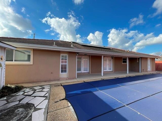 rear view of house with a covered pool, a patio, and solar panels