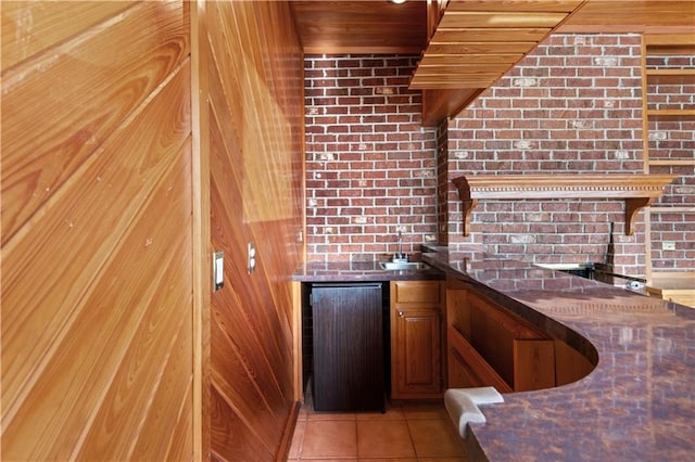 bar featuring light tile patterned flooring, brick wall, and refrigerator