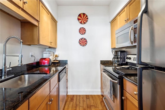 kitchen with sink, appliances with stainless steel finishes, dark stone counters, and light hardwood / wood-style floors