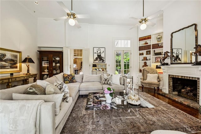 living room featuring a towering ceiling, ceiling fan, a fireplace, built in features, and ornamental molding