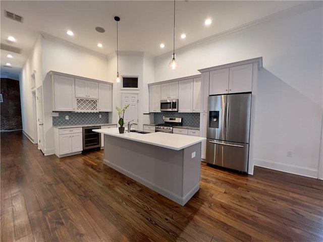 kitchen with appliances with stainless steel finishes, beverage cooler, dark hardwood / wood-style floors, decorative light fixtures, and a kitchen island with sink