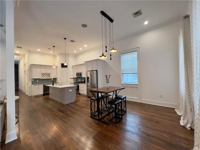 kitchen featuring appliances with stainless steel finishes, pendant lighting, a center island, backsplash, and dark hardwood / wood-style floors