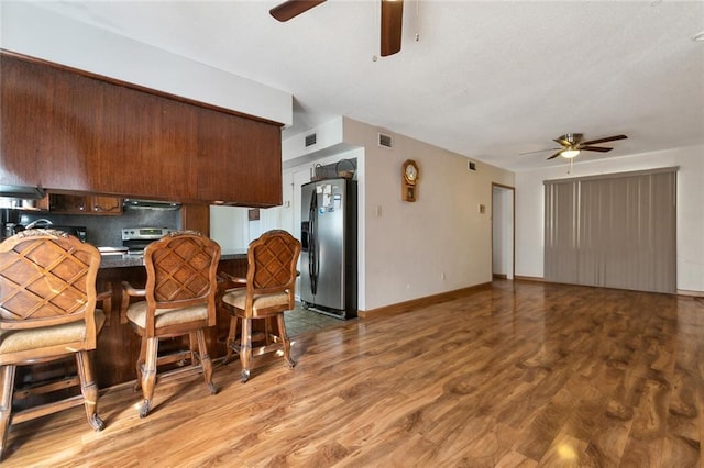 kitchen featuring kitchen peninsula, extractor fan, wood-type flooring, appliances with stainless steel finishes, and a breakfast bar area