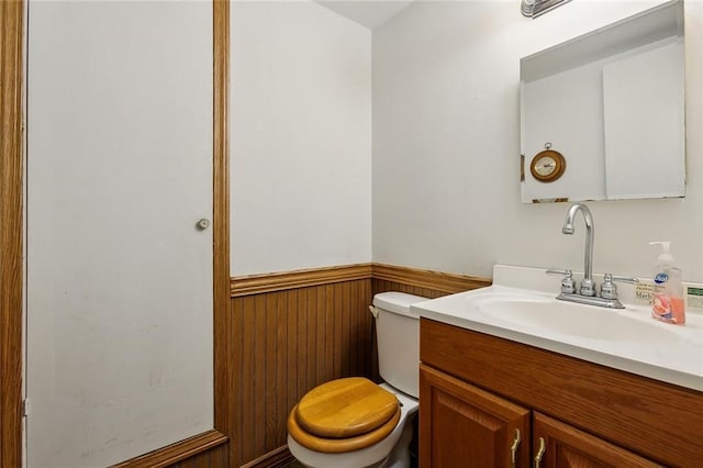 bathroom featuring wooden walls, vanity, and toilet