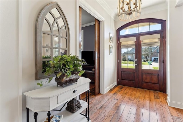 foyer featuring a chandelier, ornamental molding, light wood-type flooring, and baseboards