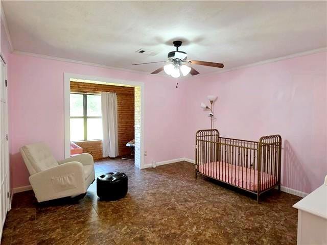 bedroom with ceiling fan, a nursery area, and ornamental molding