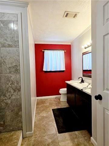 bathroom featuring toilet, tiled shower, crown molding, and vanity