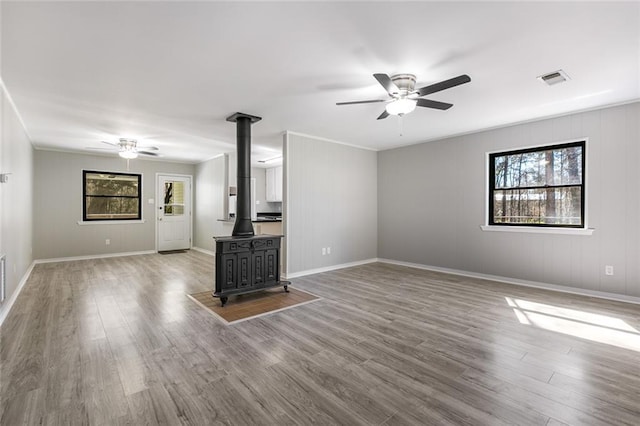 unfurnished living room featuring ornamental molding, ceiling fan, a wood stove, and hardwood / wood-style floors