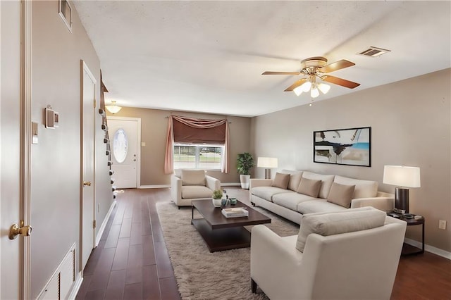 living room featuring visible vents, baseboards, dark wood-type flooring, and ceiling fan