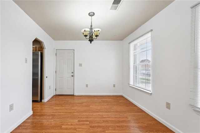 unfurnished dining area with visible vents, baseboards, arched walkways, an inviting chandelier, and light wood-type flooring