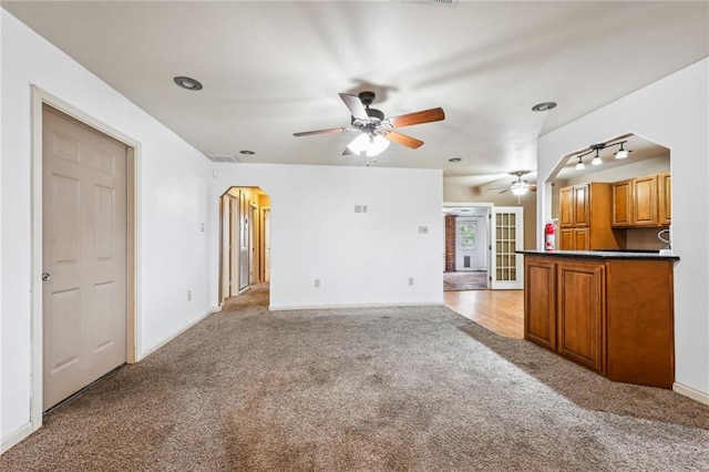 unfurnished living room with arched walkways, ceiling fan, and light colored carpet