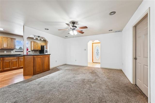 kitchen featuring arched walkways, stainless steel refrigerator with ice dispenser, brown cabinetry, open floor plan, and light carpet