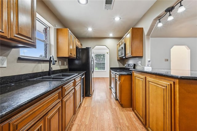 kitchen with appliances with stainless steel finishes, brown cabinetry, a sink, and dark stone countertops